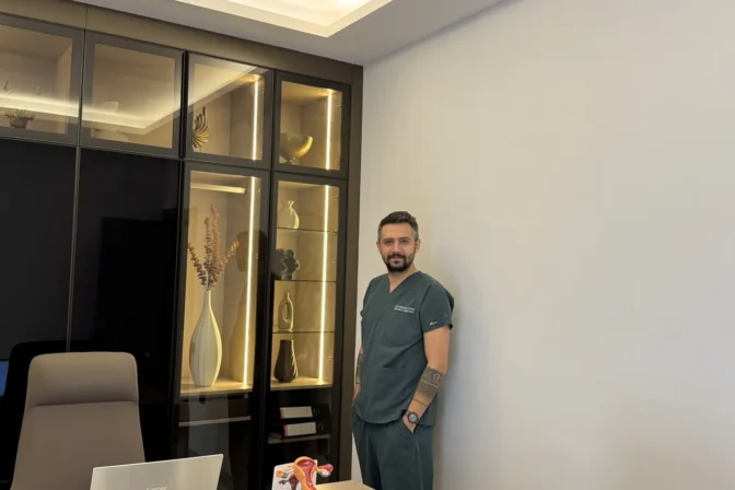 Op. Dr. Hüseyin Efe Akalın standing in the consultation room, close framing
